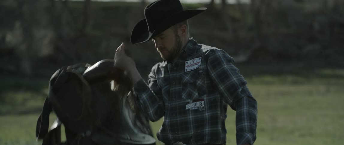 A man is carrying a saddle over a field before putting it down