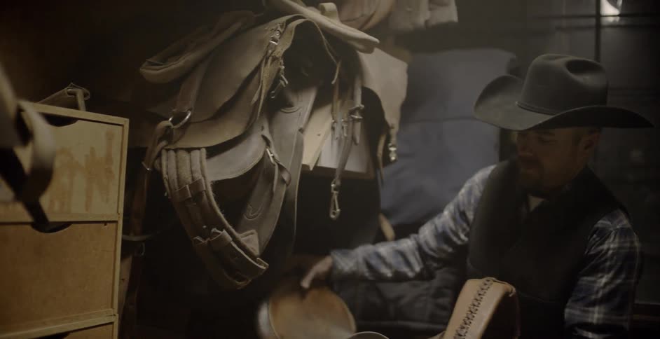A cowboy picks a saddle up off a rack