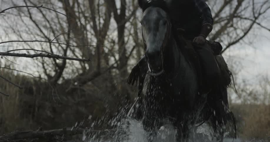 Cowboy riding a horse down a shallow stream on a cloudy winter day