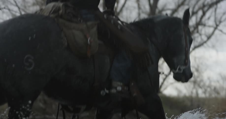 Cowboy riding a horse down a shallow stream on a winter day