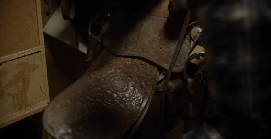 A man walks through his barn to pick up his saddle