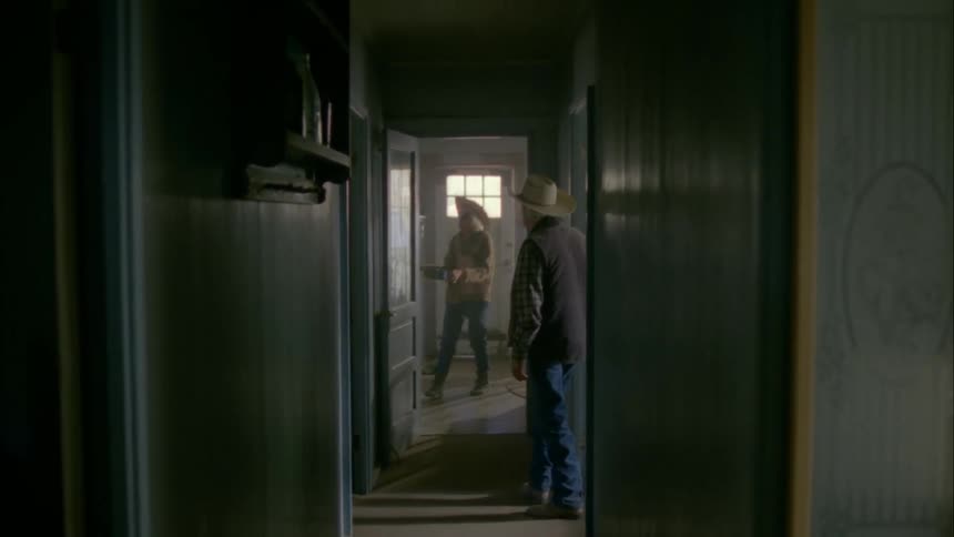 An elderly couple wear cowboy hats and walk through a hallway