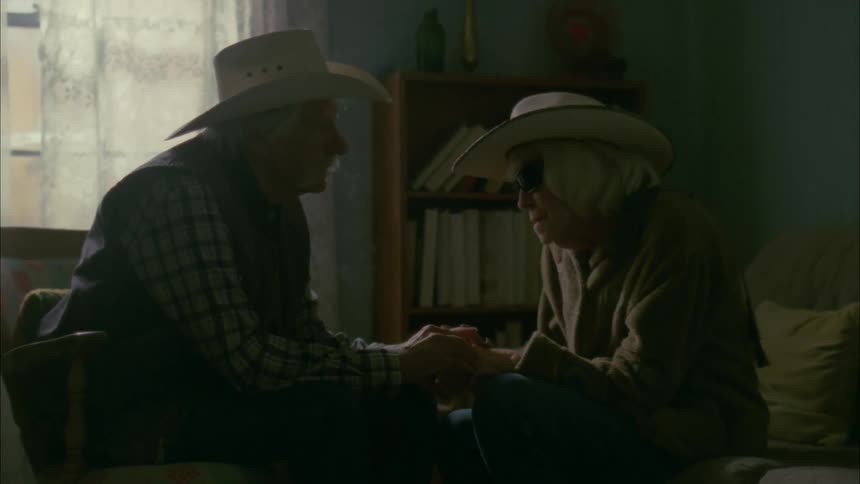 Elderly couple holds hands sitting in a living room