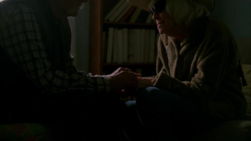 Elderly couple holds hands sitting in a living room