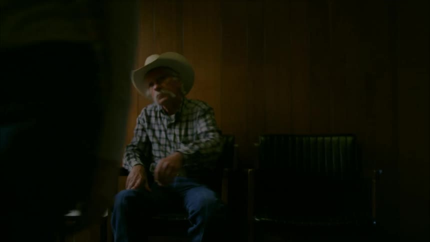 An elderly couple hold hands while sitting in a waiting room and then the woman walks away