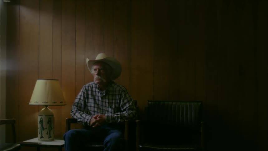 An elderly man in a cowboy hat sits in a waiting room