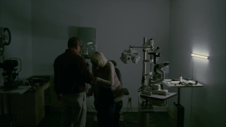 Optometrist leads elderly lady to a seat in his office