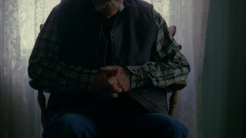 Older man sitting still in chair next to window