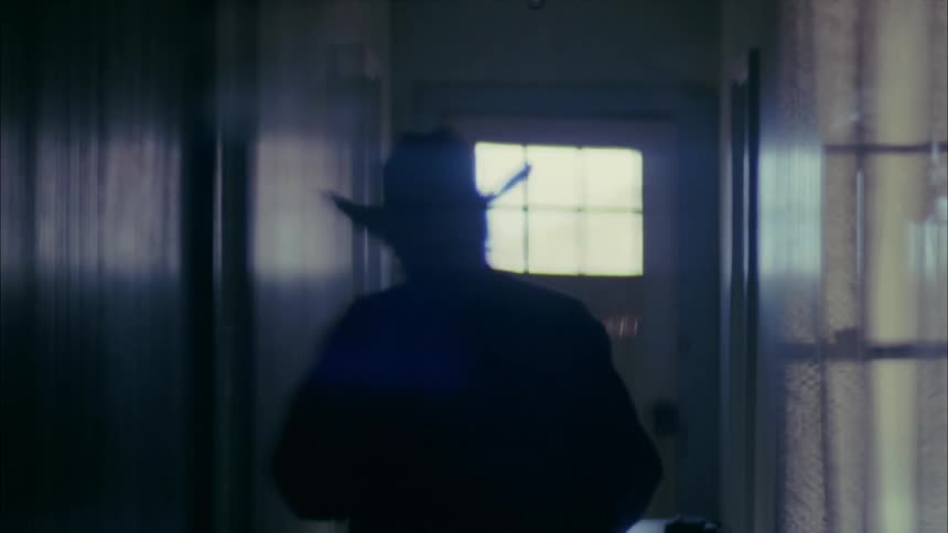 Elderly man walks down the hallway of his house and into a room