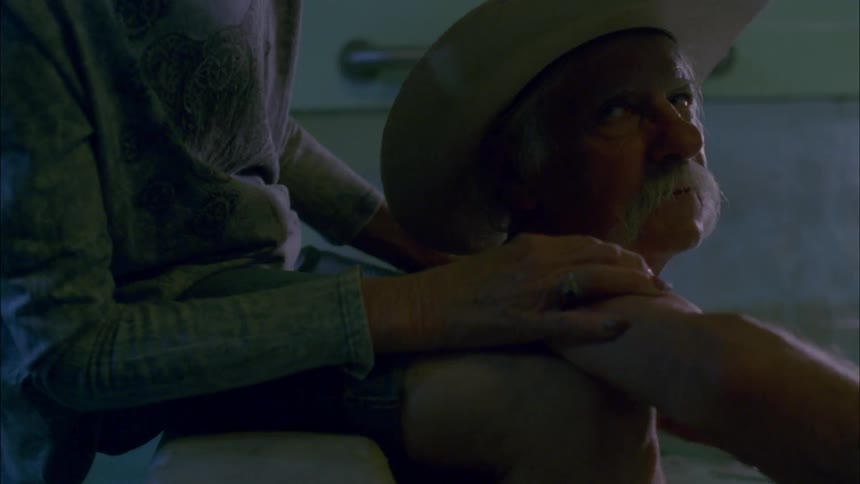 Woman rubs elderly mans shoulders as he sits in water