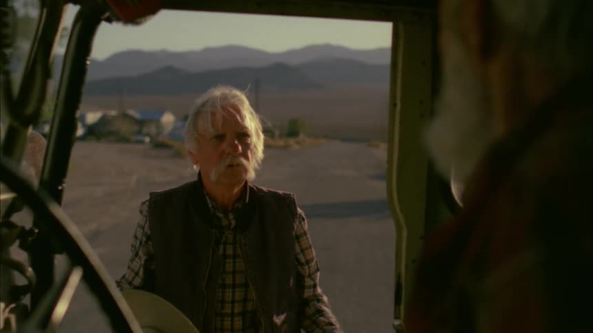 A man with a mustache talks to a bearded man in a truck
