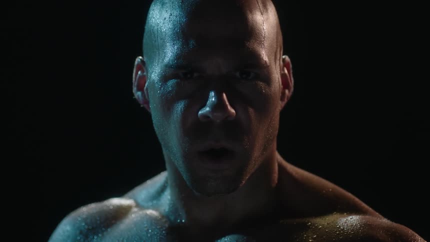 Muscular bald man breathing while stationary as beads of sweat are upon him