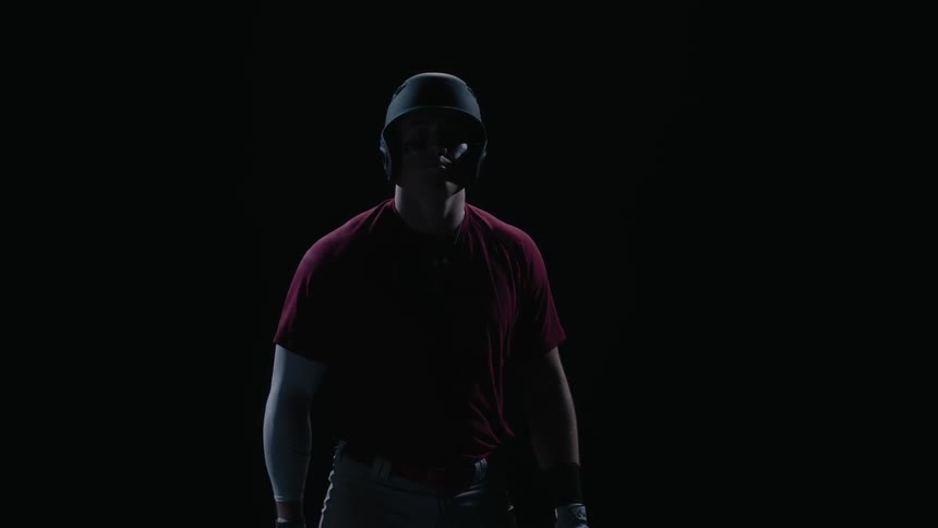 A man walks up with a bat and helmet in the dark