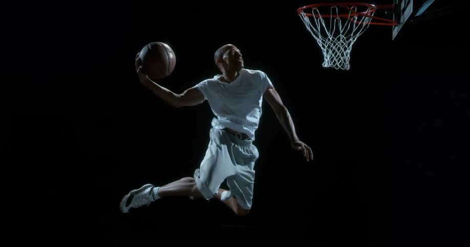 Black male with a basketball jumps up to dunk the ball into the net