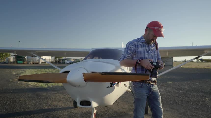 A man playing with a camera while he is standing next to a plane at an airport