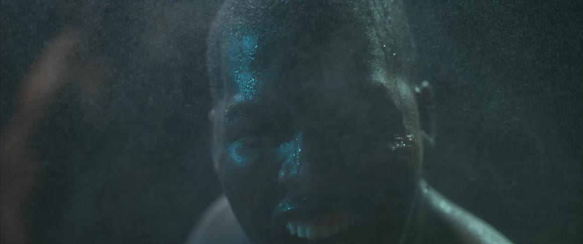 A man covered in sweat with mist floating by is staring aggressively into the camera