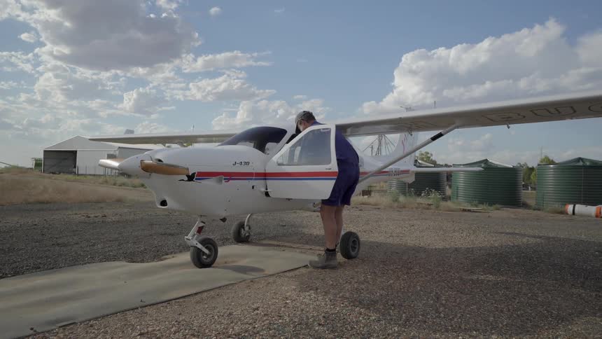 Men climb into a small airplane in a rural area