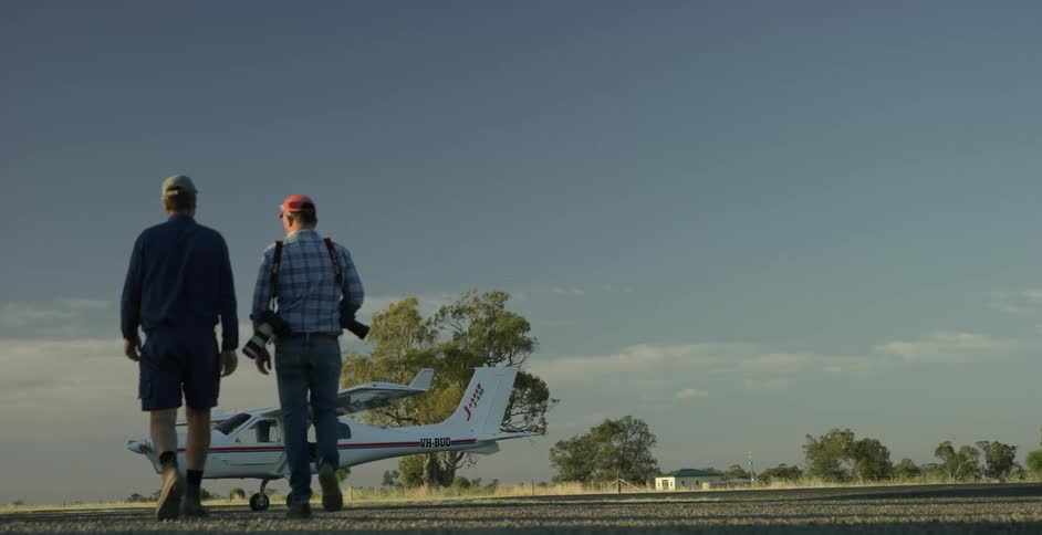 Two men, one carrying cameras, walk towards a small plane
