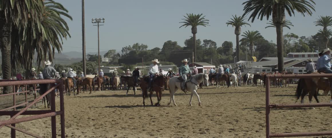 Cowboys ride horses in a paddock