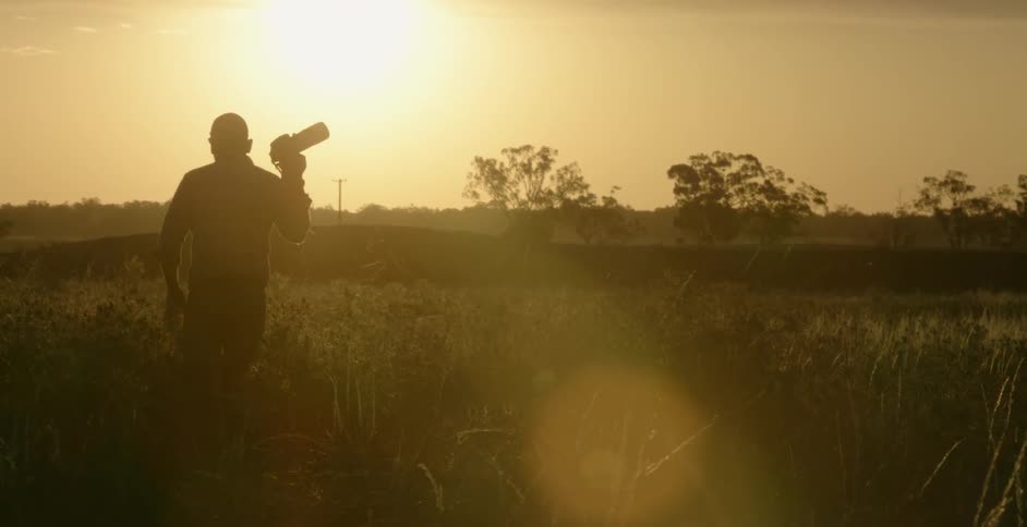 A photographer walks in a field carrying a camera