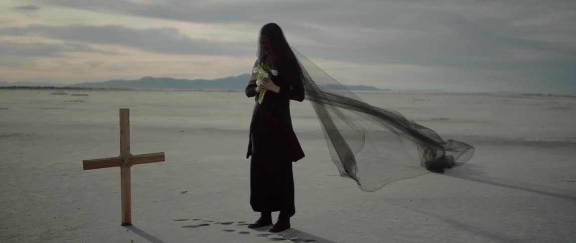 A woman grieves at a cross wearing black lace