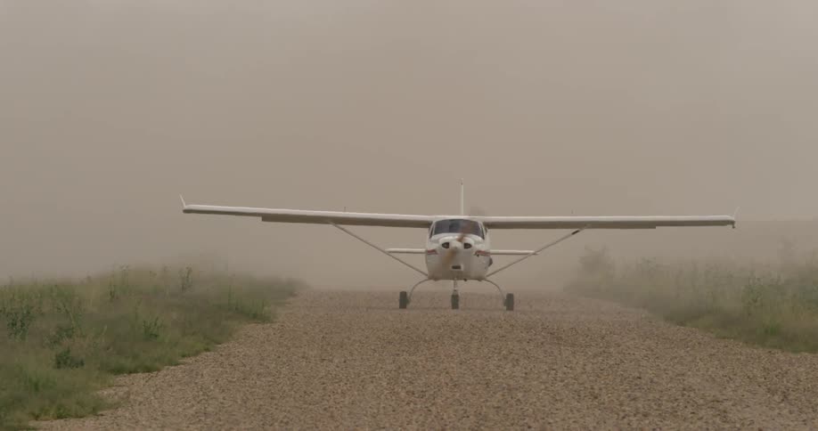A small plane kicks up dirt on a gravel runway