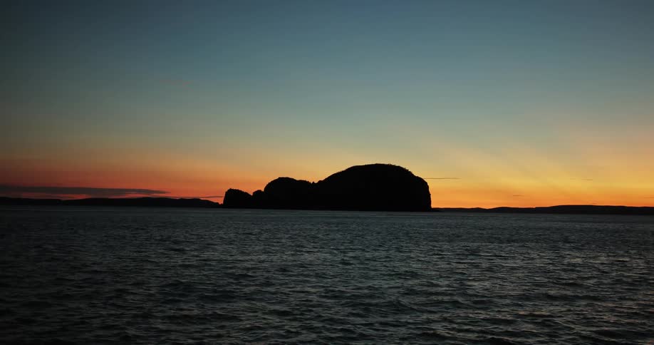 The sun setting behind a large rock out on the ocean