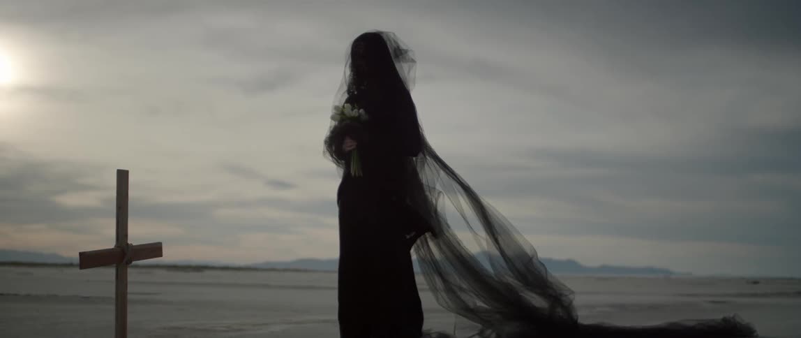 A woman is standing near a grave on a windy day
