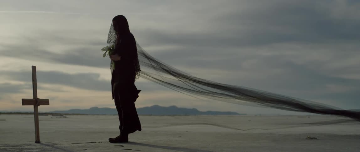 The wind blows the long veil of a woman dressed in black