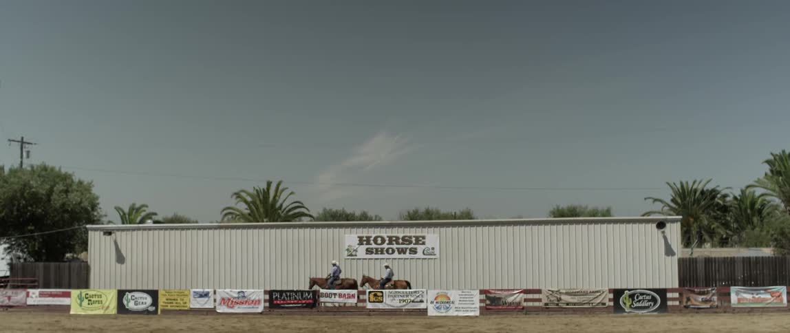 Men ride horses past a white building