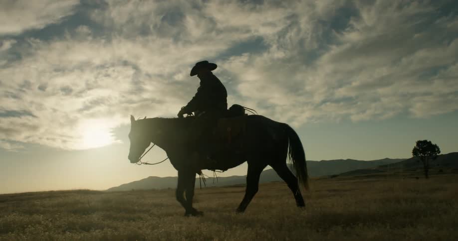 A cowboy is riding his horse over a grassy plain on a cloudy day