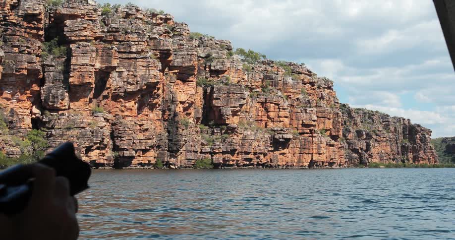 A person is taking photos as their boat passes by jagged cliffs