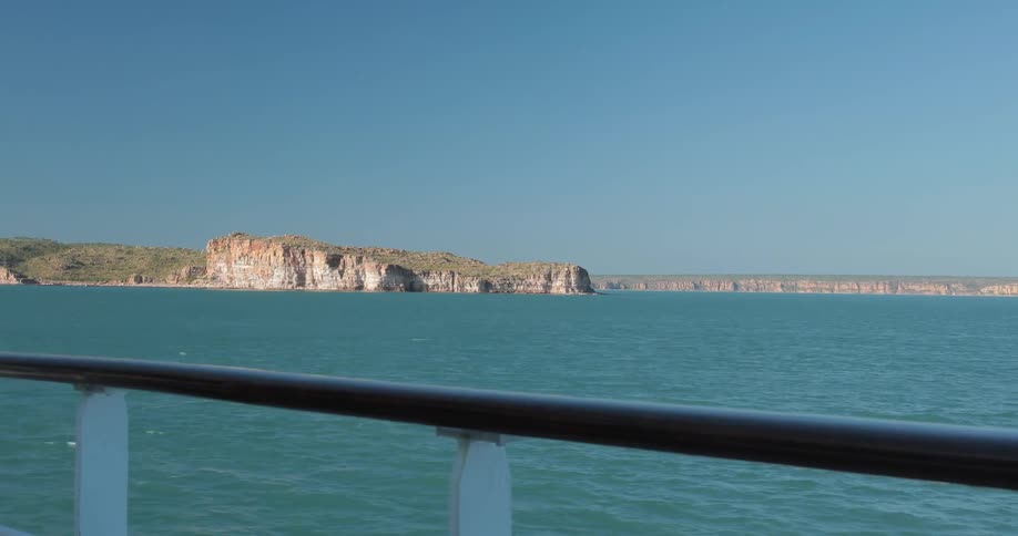 A boat is traveling off a coastline on a sunny day