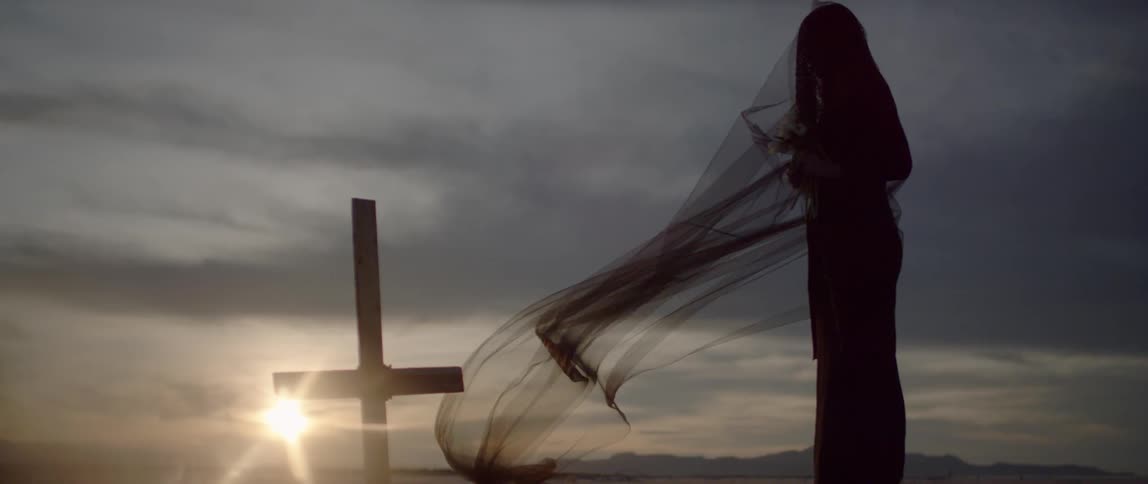 A woman stands near a grave at sunset