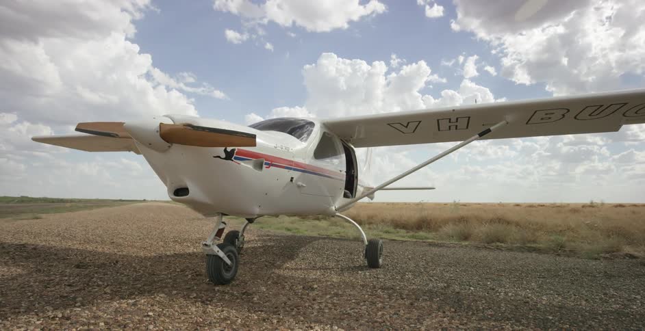 A small propeller plane sits on a rural airstrip