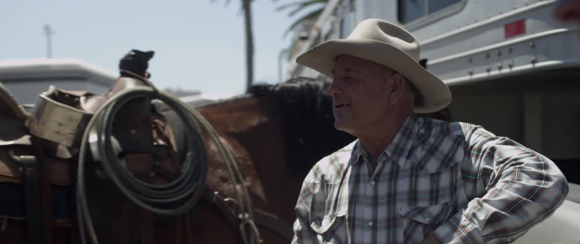 Two cowboys shake hands near a horse