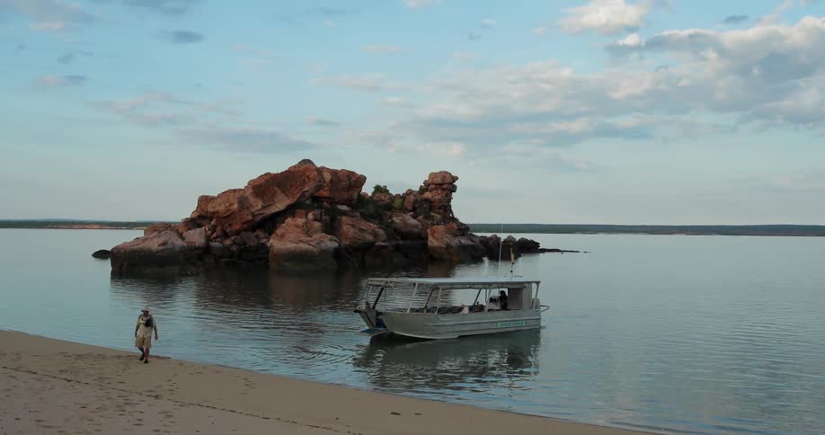 Boat pulls away from shore and a man walks on the beach