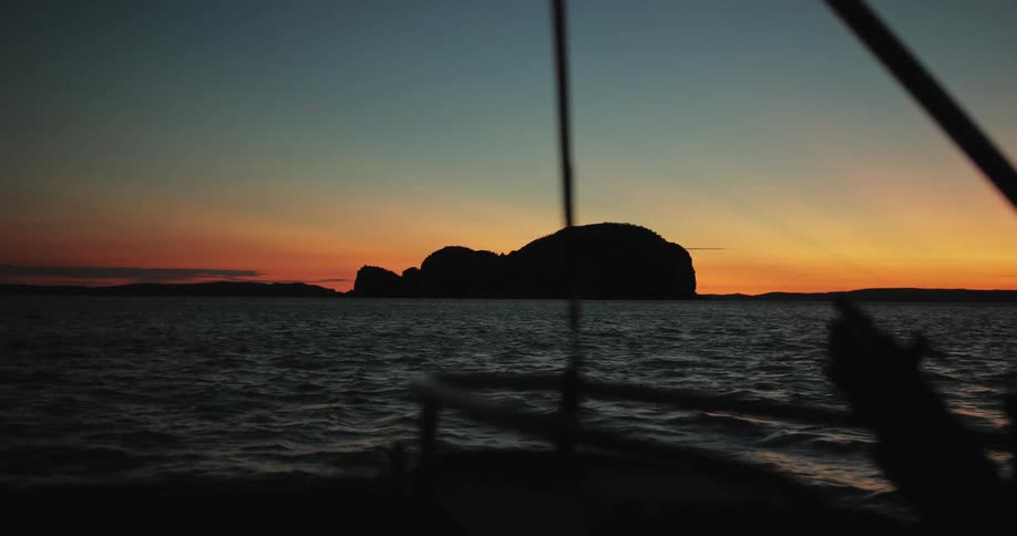 A boat is sailing near an island at dusk
