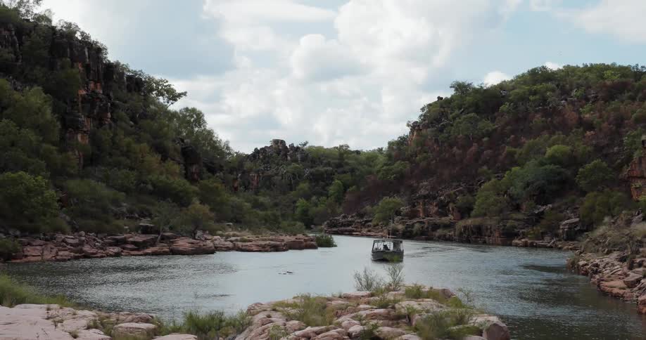 A boat travels down a river between tree covered rocks