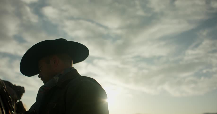 Man wearing a hat sits on a horse in the sun