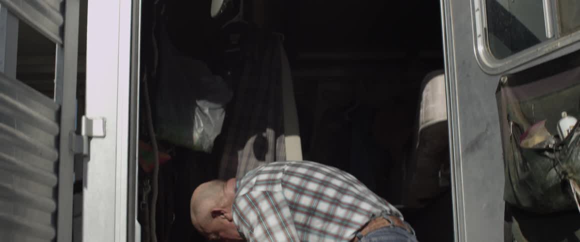 A man removes a cowboy hat and grabs some rope
