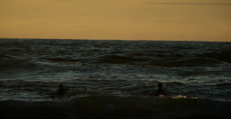 Surfers float on surfboards in the ocean at sunset