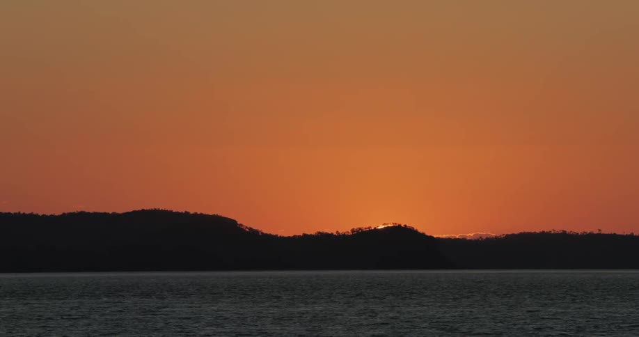 Sun sets behind island and flowing water