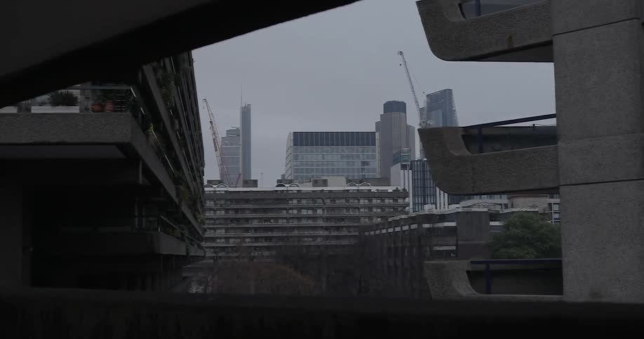Cranes are seen rising over tall buildings in a city on an overcast day