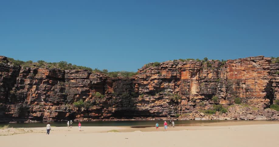 People wander around and stand on a beach near some cliffs