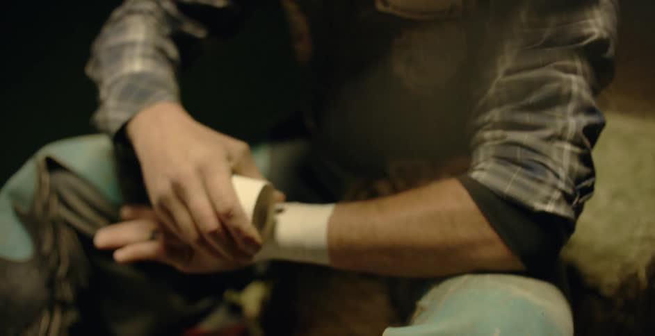 Man wearing a cowboy hat sits and wraps his hand