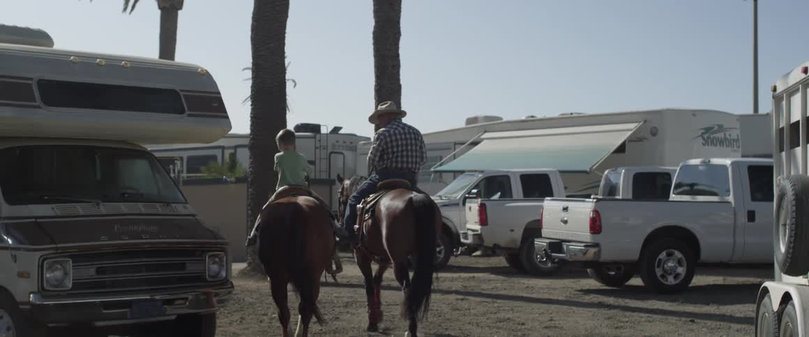 Man and child ride horses near camping vehicles