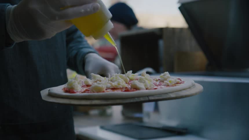 A restaurant worker drizzles oil over an uncooked pizza