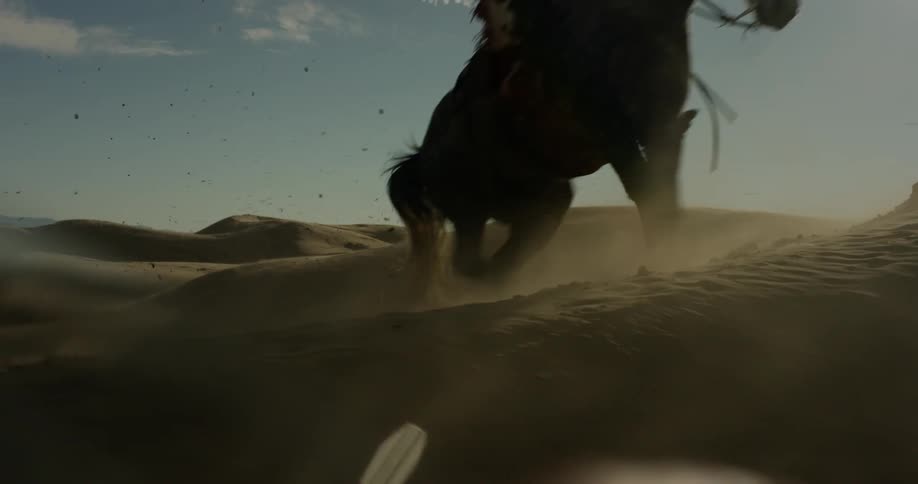 Man riding horse up sand dune hill on windy day