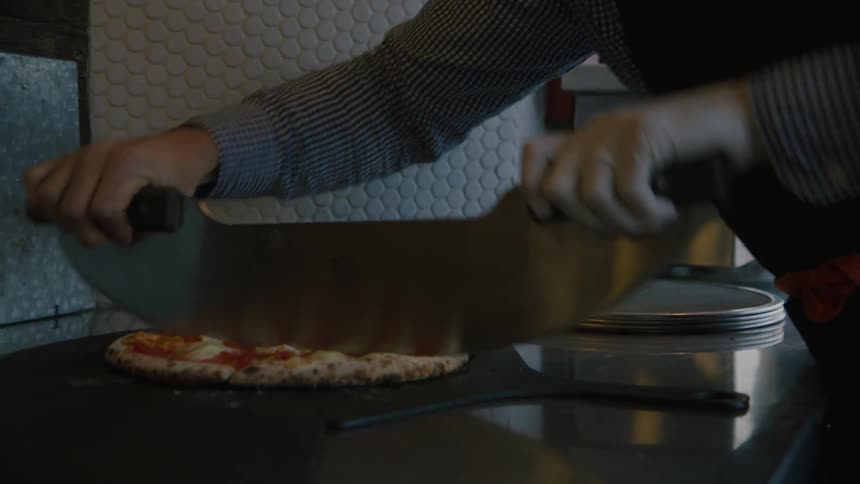 A restaurant worker cuts up a cooked pizza